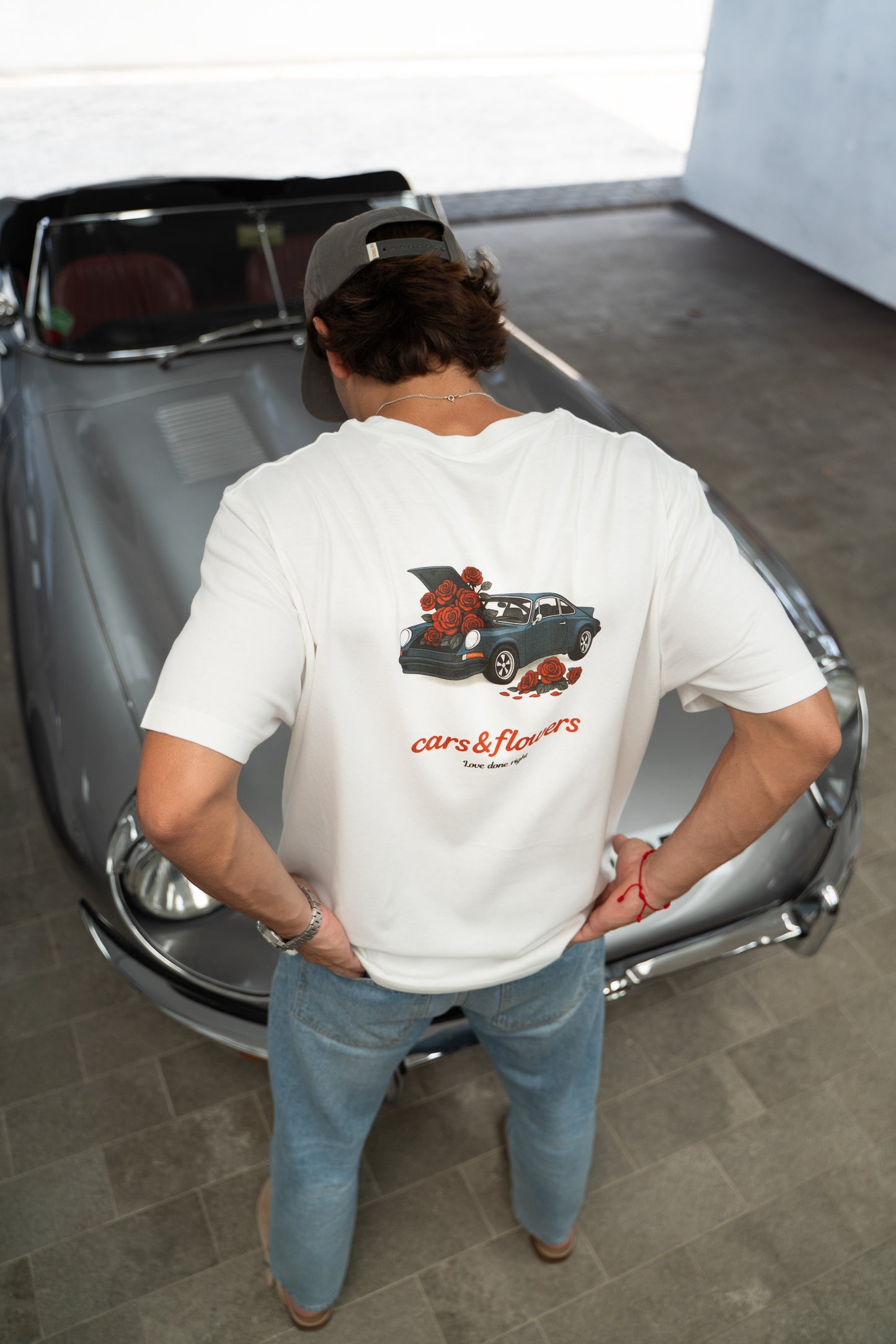 Model wearing a white t-shirt with a classic Porsche 911 design, standing in front of a vintage car.