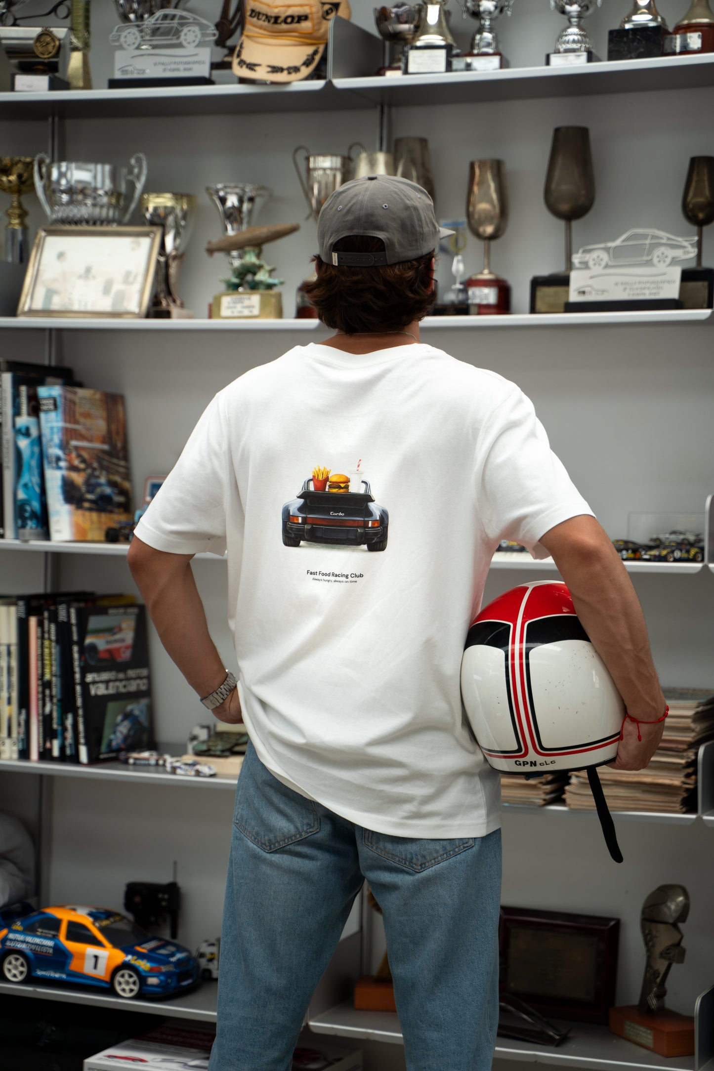 Person wearing a white t-shirt with a porsche 911 turbo car design, holding a helmet